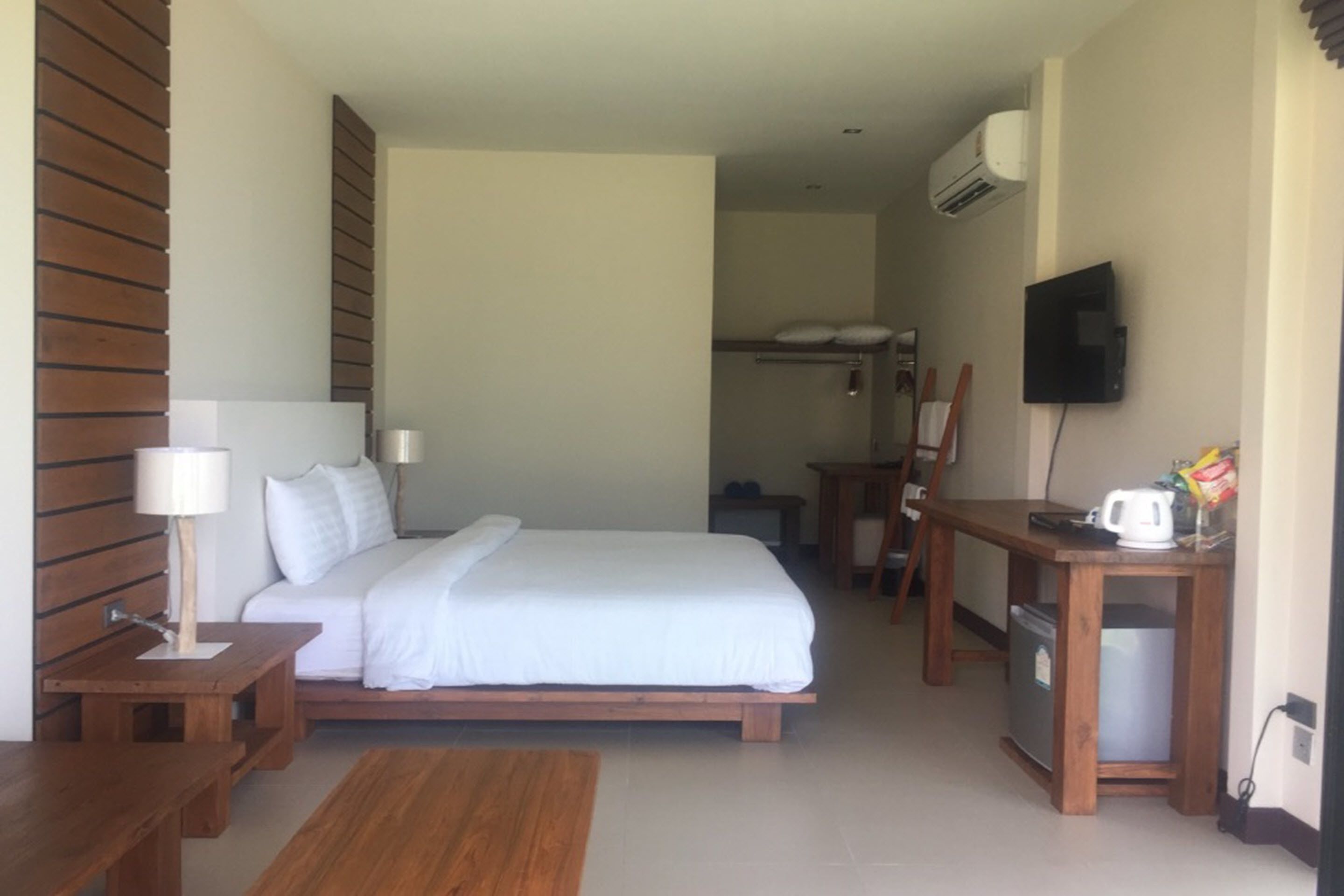 A hotel room with a bed, wooden furniture, a television, and a kitchenette.