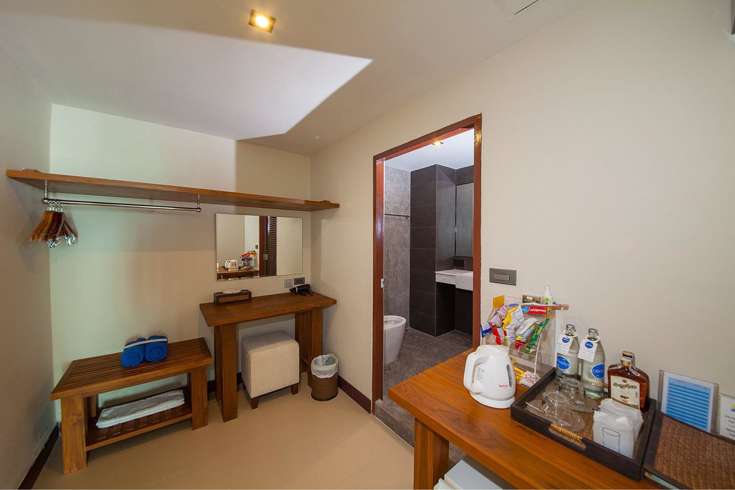 Un baño moderno con tocador de madera, un espejo, un perchero y una bandeja con artículos de aseo.