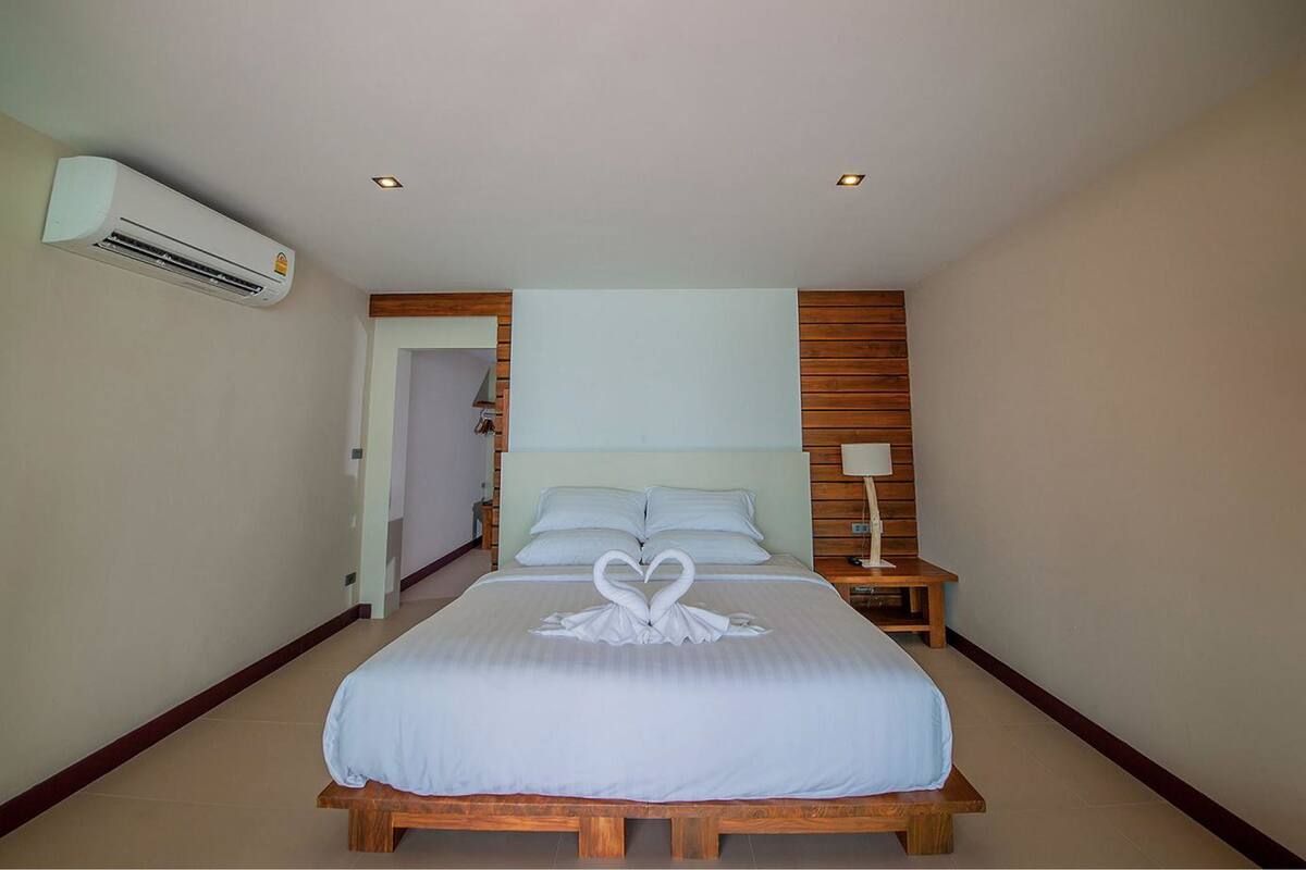 A hotel room with a bed, a nightstand, an air conditioning unit, and a wooden headboard.