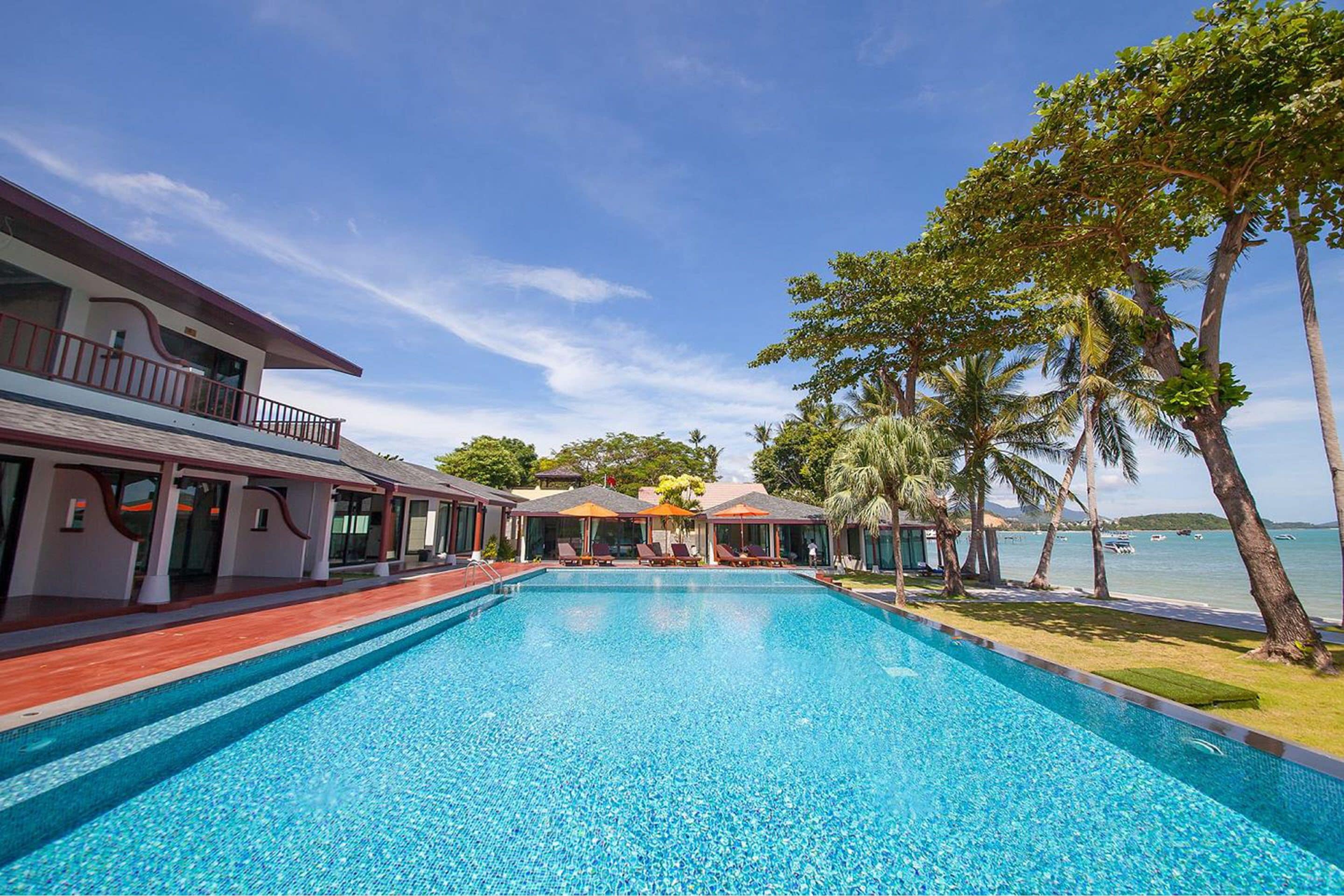 Una piscina con vista al mar, rodeada de palmeras y un edificio con balcón.