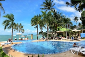 A poolside area with lounge chairs and umbrellas, surrounded by palm trees and a view of the ocean.