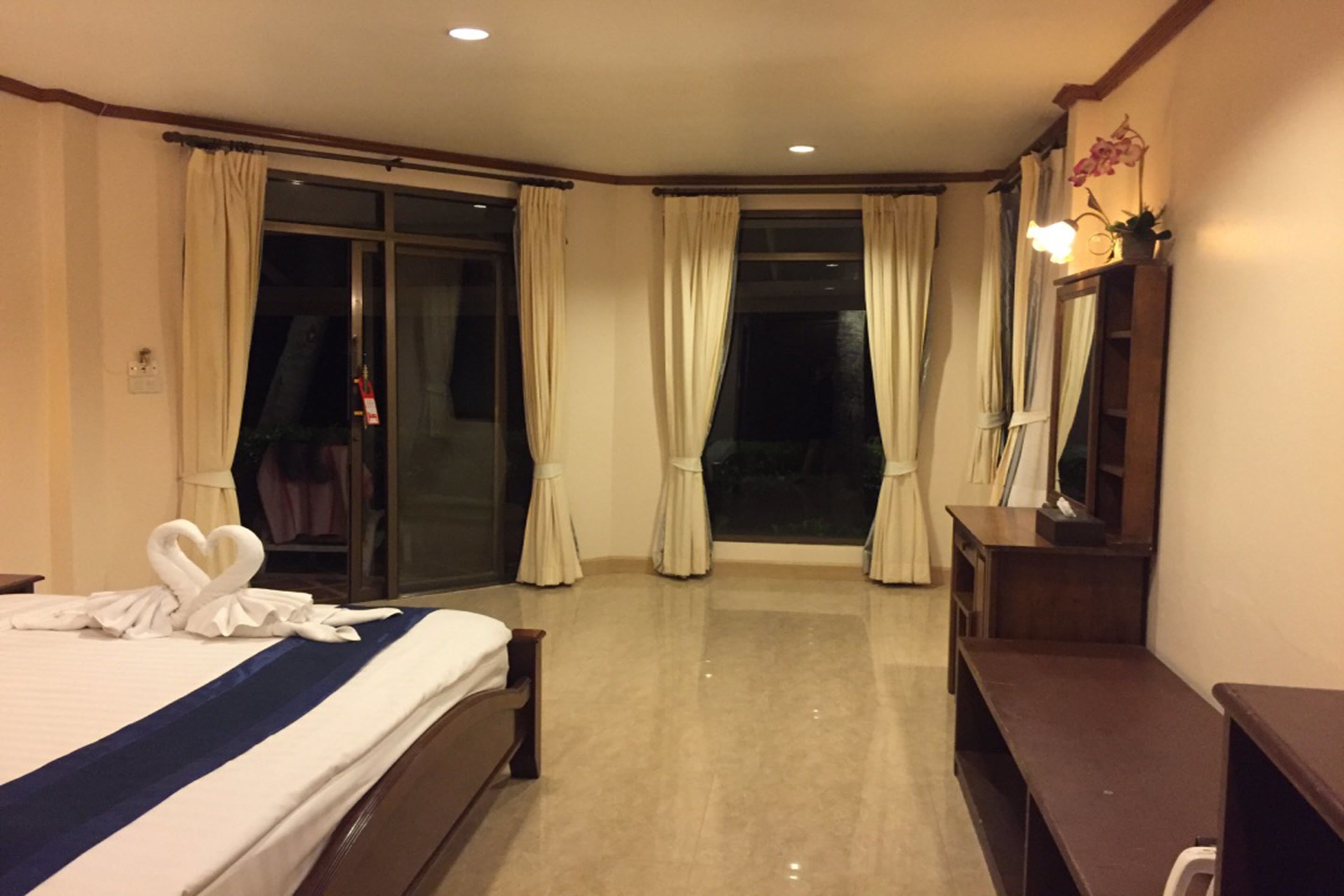 A hotel room with a large bed, a desk, a mirror, and a sliding glass door leading to a balcony.