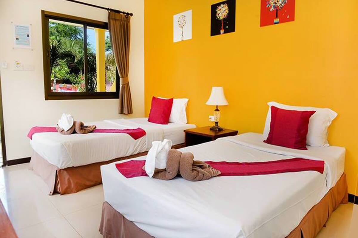 Une chambre d’hôtel avec deux lits, chacun agrémenté de draps blancs et d’oreillers rouges, une fenêtre avec des rideaux et un mur jaune orné d’œuvres d’art.