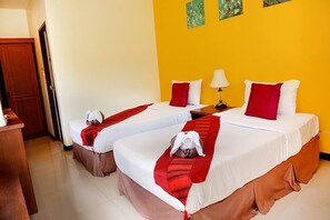 A hotel room with two beds, each with white linens and red accents, a wooden desk, and a yellow wall with floral artwork. - Samui Mermaid Resort Garden Side (Koh Samui)