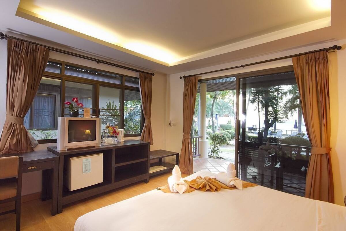 Une chambre d’hôtel comprenant un lit, un bureau avec une télévision, un petit réfrigérateur et un balcon avec des rideaux.