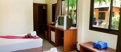 Habitación de hotel con dos camas, un escritorio con televisor y ventana con vistas a palmeras.