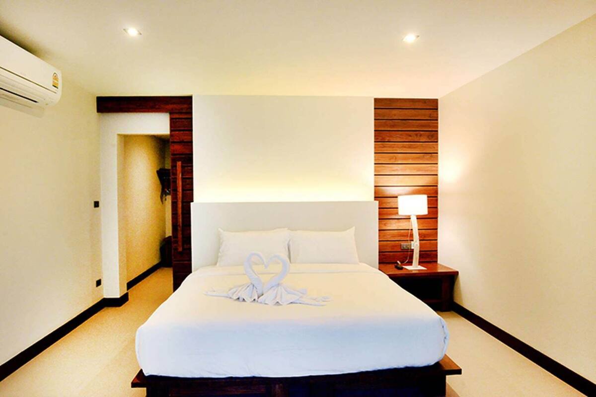 Une chambre d’hôtel avec un grand lit, une tête de lit en bois, une lampe de chevet et un appareil de climatisation.
