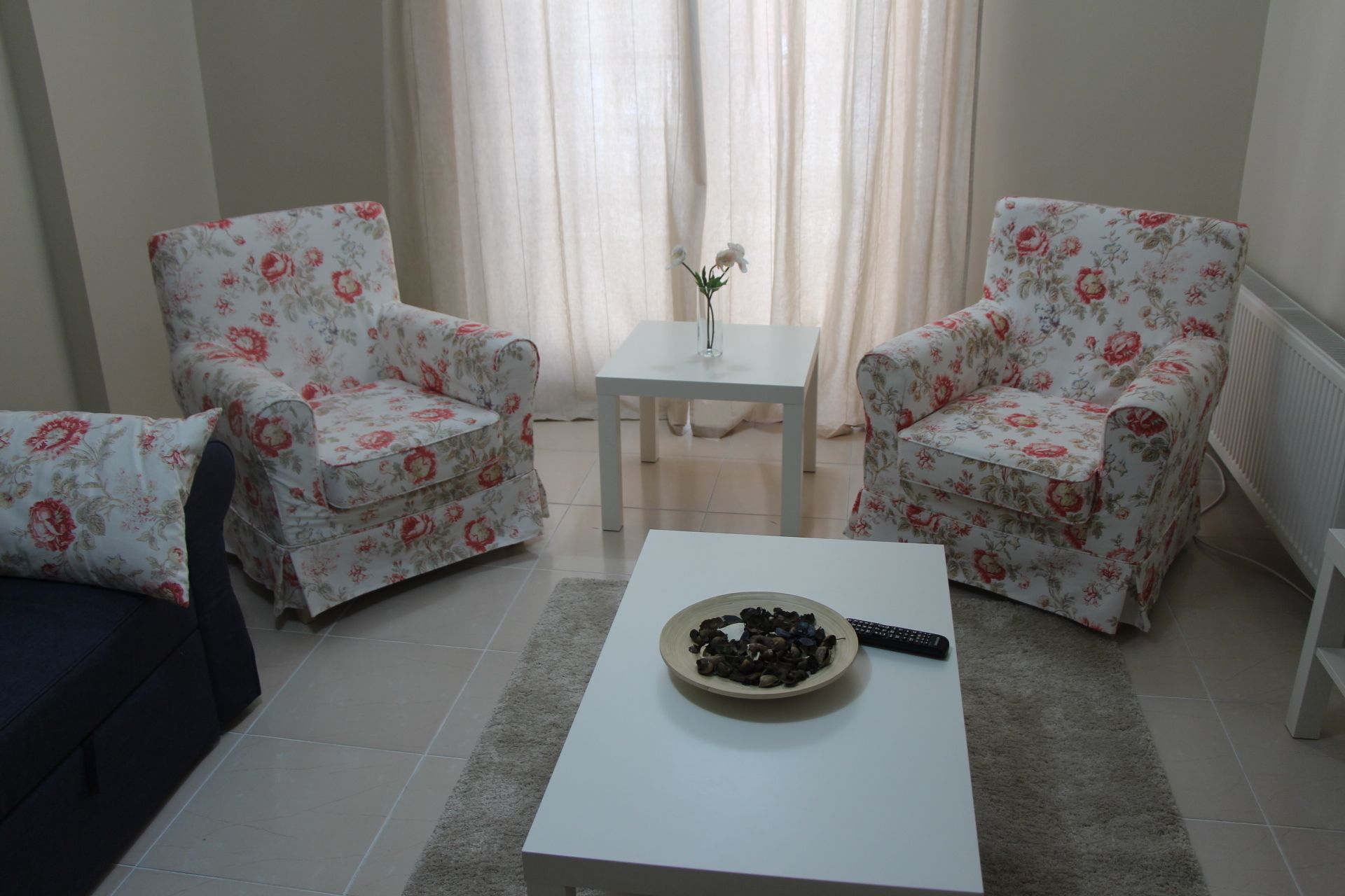 Una sala de estar con dos sillones estampados, una mesa de centro blanca y una mesita con un jarrón.
