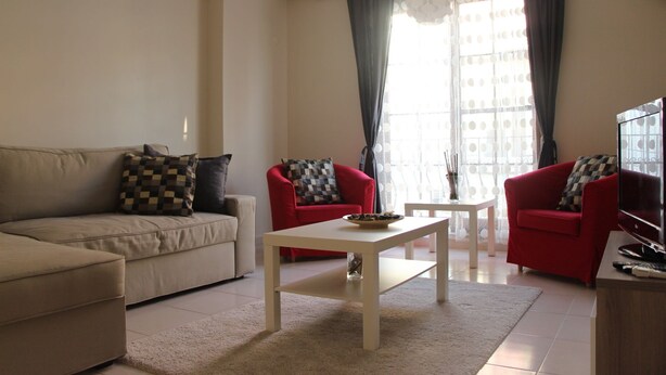 A living room with a beige sofa, two red armchairs, a white coffee table, and a TV on a wooden stand. - Kinzi House (Çanakkale)
