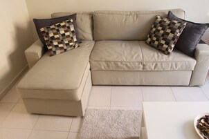 A beige sectional sofa with a matching ottoman, two patterned throw pillows, and a white coffee table with a bowl of fruit.