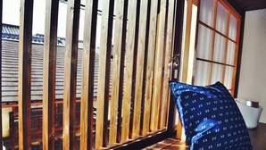A room with a wooden floor, a blue patterned pillow, and a sliding door with a view of the outside. - Chika Odoru (Kyoto)