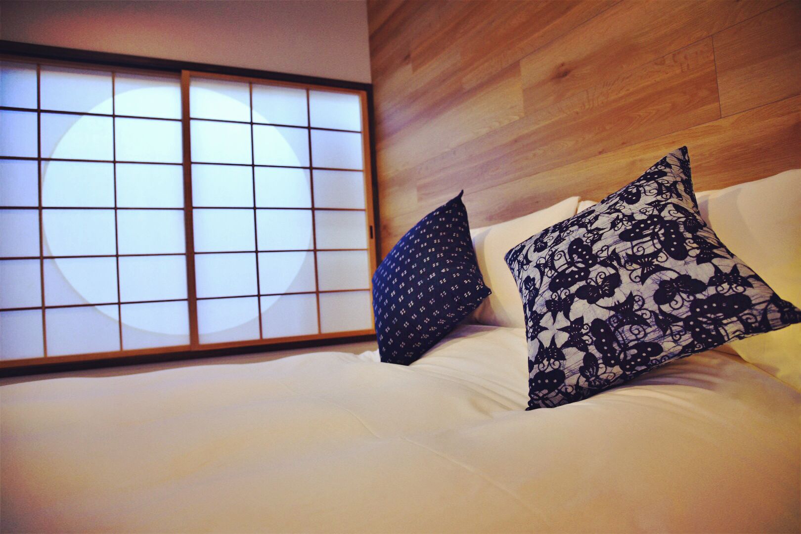 A hotel room with a large shoji screen, a bed with white linens, and two patterned pillows.