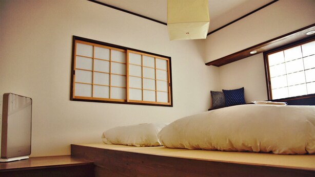 A traditional Japanese-style room with tatami flooring, a low wooden bed with cushions, a shoji screen, and a ceiling fan. - Chika Odoru (Kyoto)