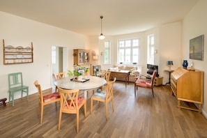 A spacious living area with a dining table, chairs, a sofa, and a wooden cabinet.