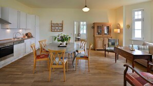 Een ruime keuken met witte kasten, een eettafel met stoelen, een houten bank en een bank.