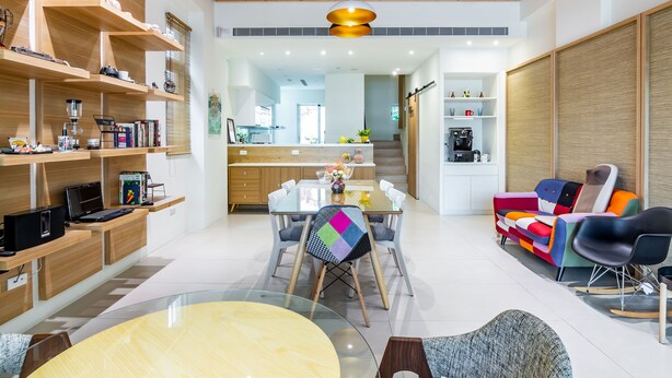 A modern kitchen with wooden shelves, a dining table, and a colorful sofa. - Angel Pension (Taitung)
