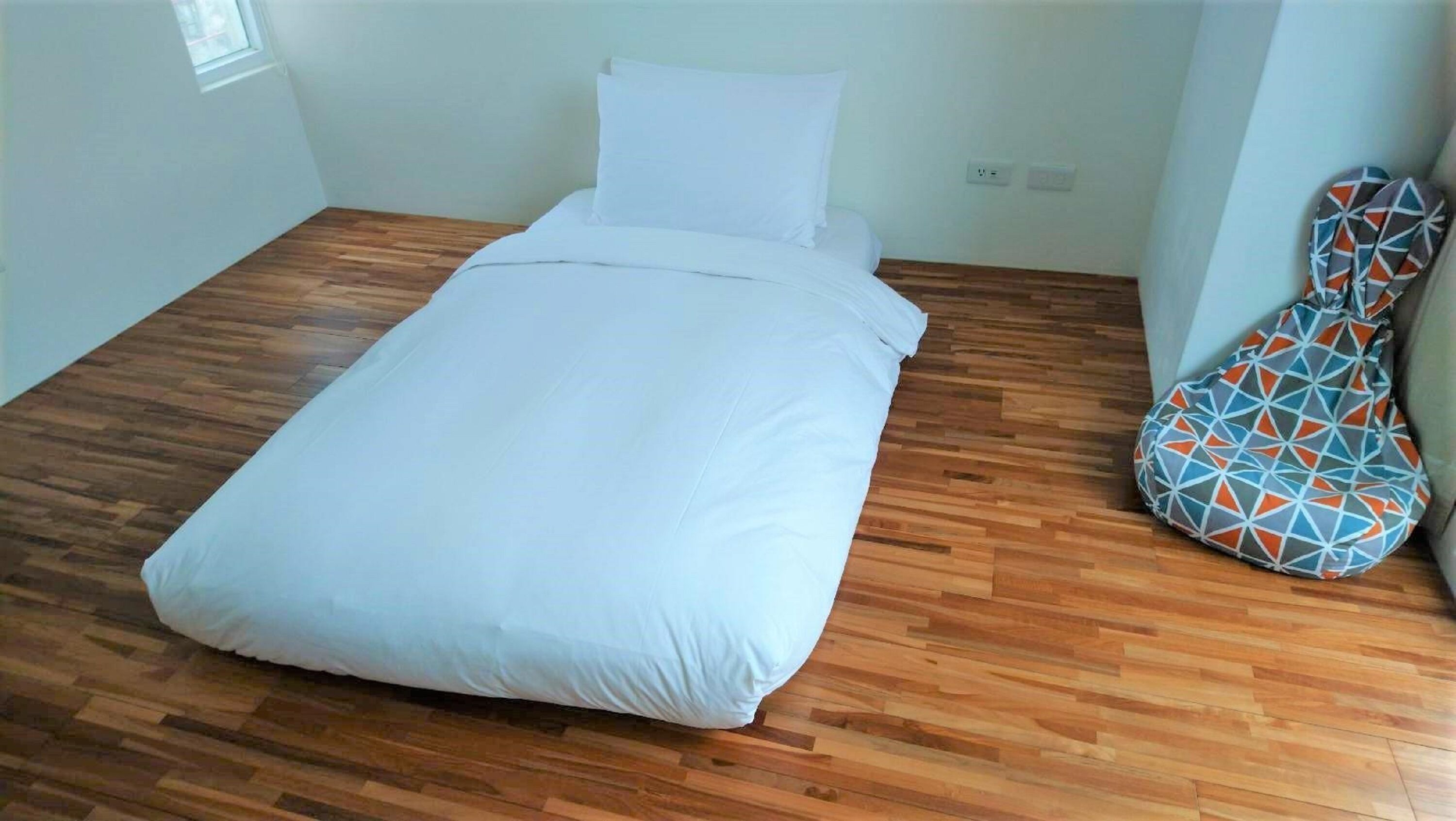 Una habitación con una cama, suelo de madera, un ventanal y una funda para guitarra.