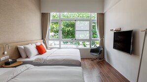A hotel room with two beds, a TV, a chair, and a window with a view of greenery. - Angel Pension (Taitung)