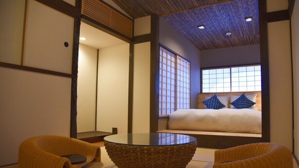 A traditional Japanese-style room with tatami flooring, a low table, and a bed with blue pillows. - Chika Yusen (Kyoto)