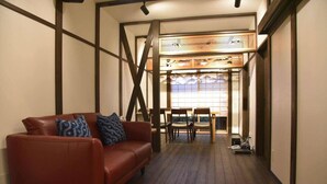 A modern interior with a leather sofa, wooden dining table, and a view through a large window. - Chika Yusen (Kyoto)