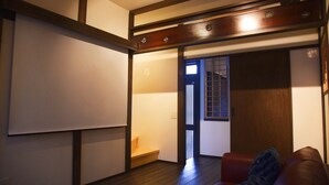 A room with a wooden floor, a red sofa, a sliding door, and a whiteboard on the wall. - Chika Yusen (Kyoto)