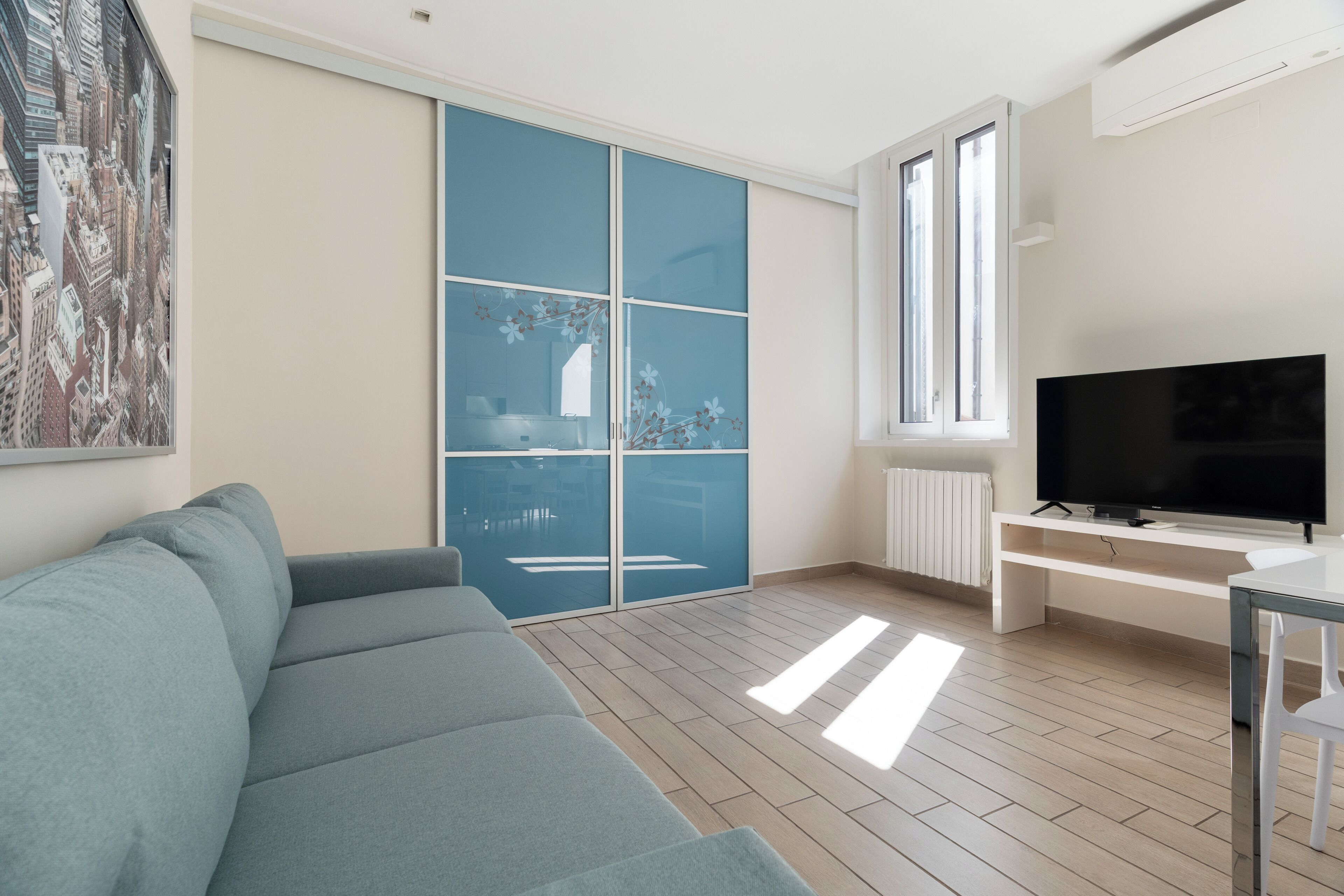 Un moderno salón con sofá, televisor, ventana grande y puerta corrediza con vista a la ciudad.
