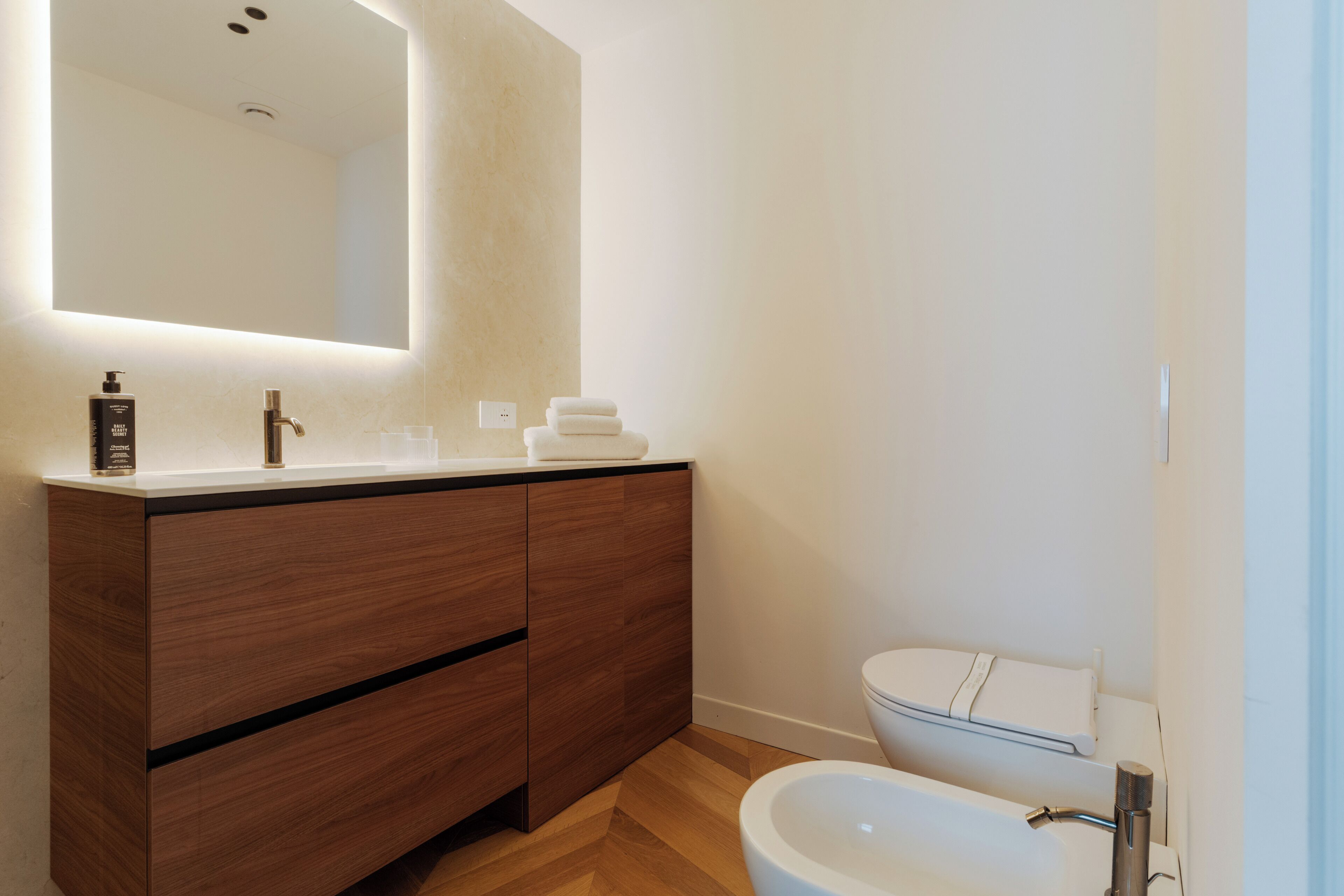 A modern bathroom with a wooden vanity, a large mirror, a white sink, and a toilet.
