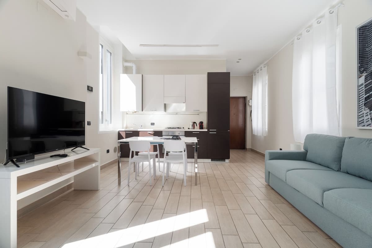 A modern living room with a flat-screen TV, a sofa, and a dining area with chairs and a table.