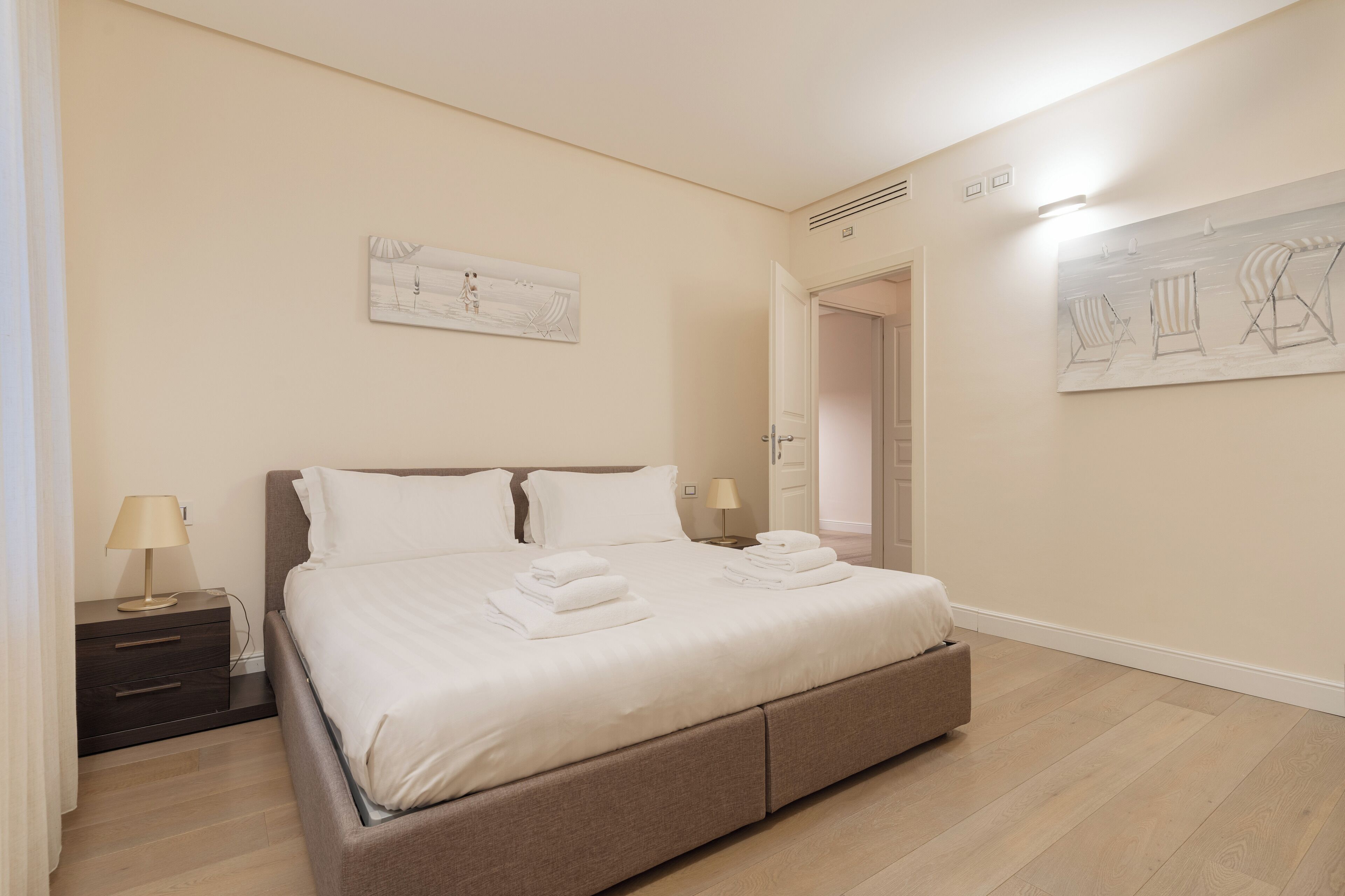 A bedroom with a bed, nightstands, and artwork on the walls.