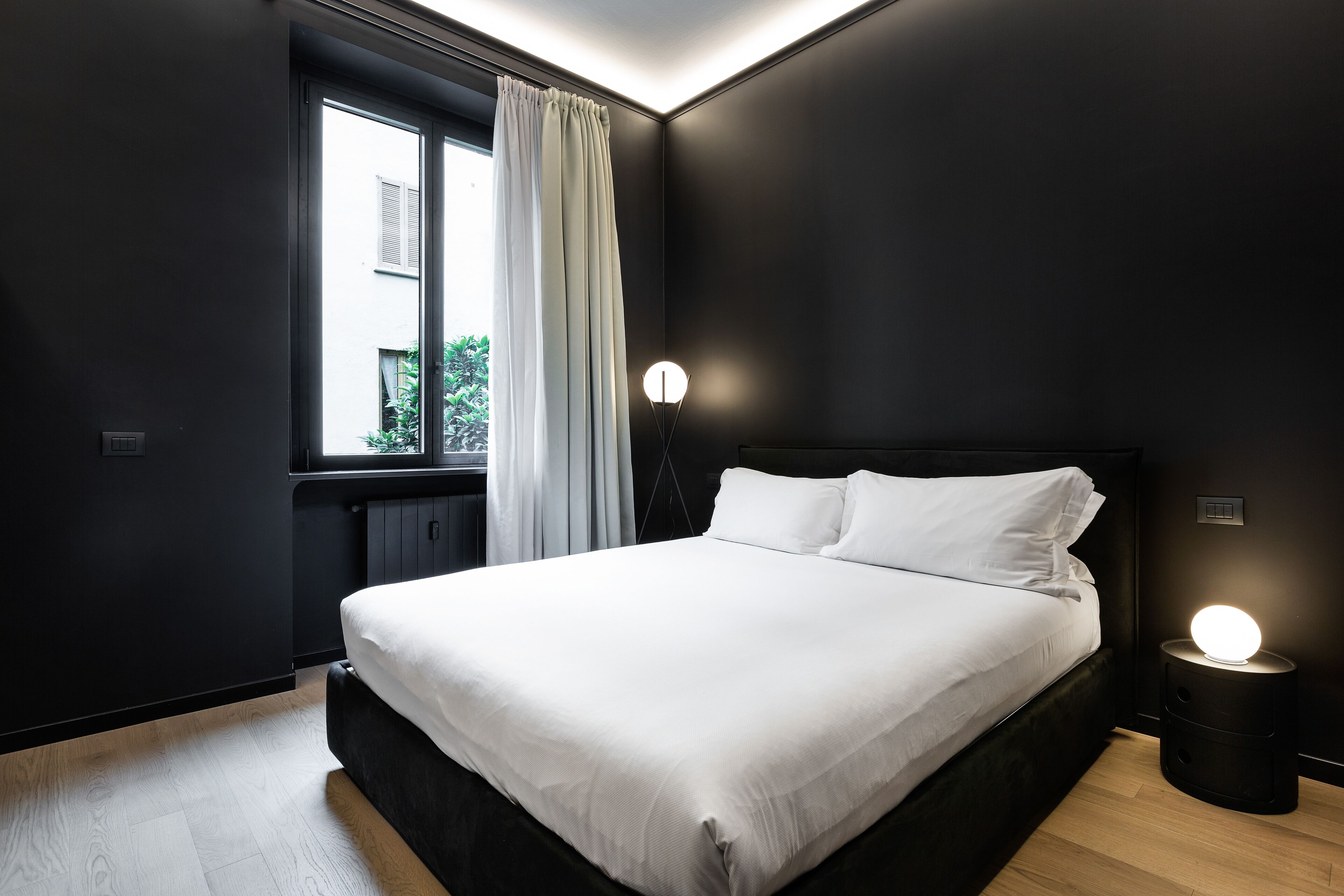 A modern bedroom with a large bed, a window with curtains, and a bedside lamp.