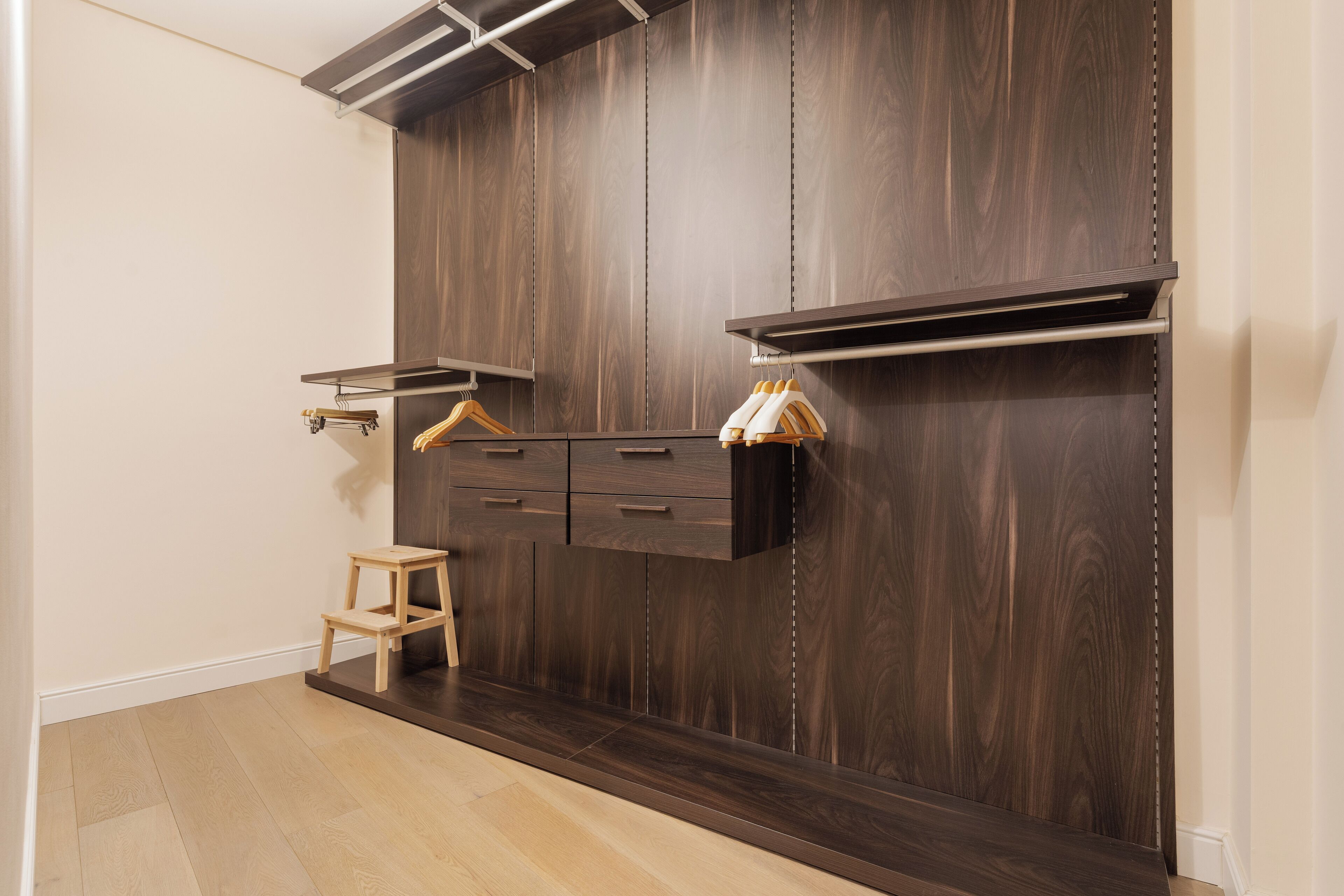 A room with a dark wood panel wall, a small wooden stool, and a shelf with hanging items.