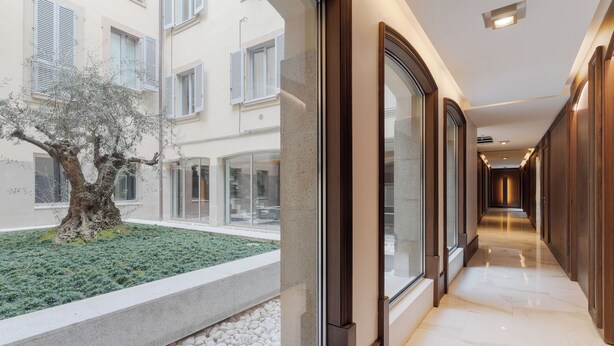 A corridor with a glass wall, a tree, and a stone pathway. - Brera Apartments in City Center (Milan)