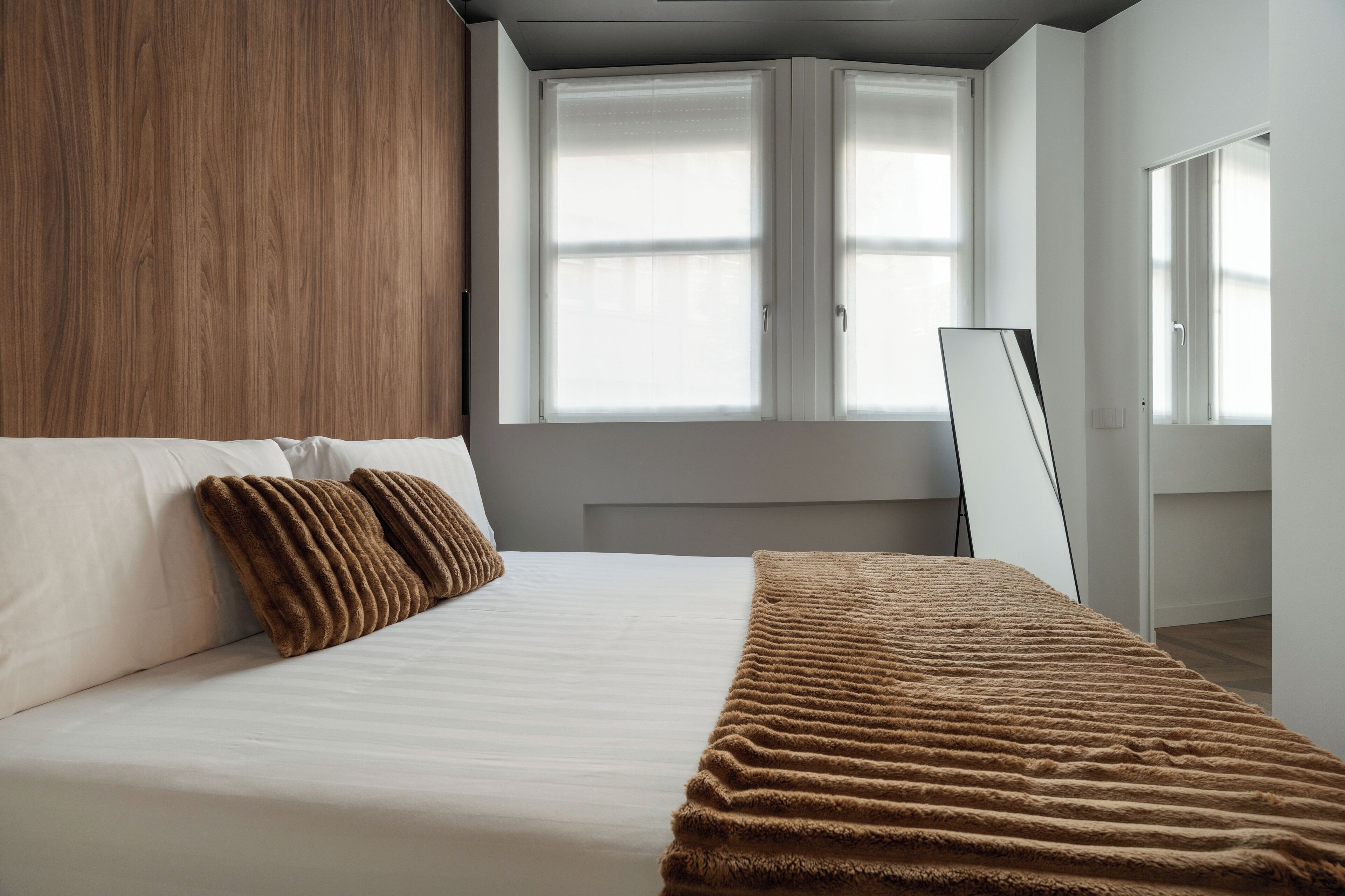 A bedroom with a bed, two pillows, a blanket, a window, and a mirror.