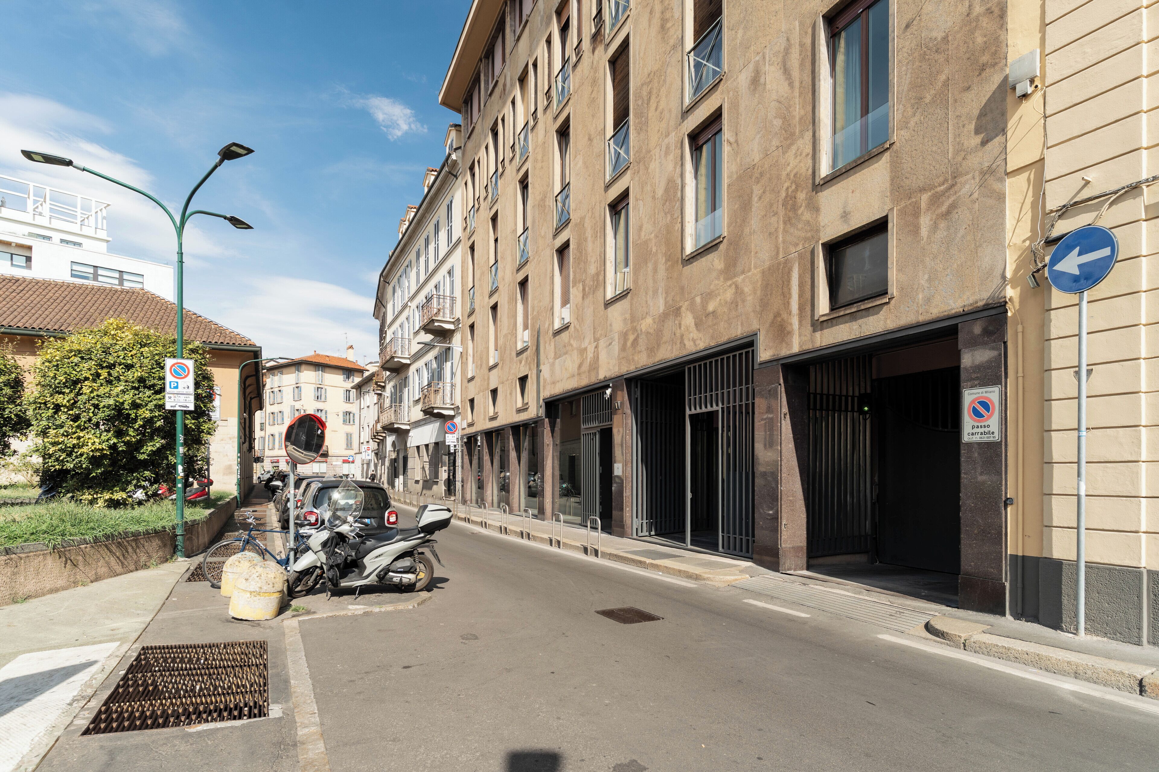 A street with parked scooters, a no parking sign, and a building with barred windows.