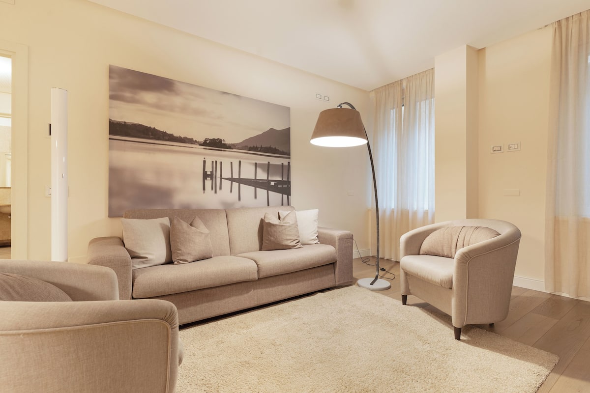 A modern living room with a beige sofa, a matching armchair, and a large floor lamp.