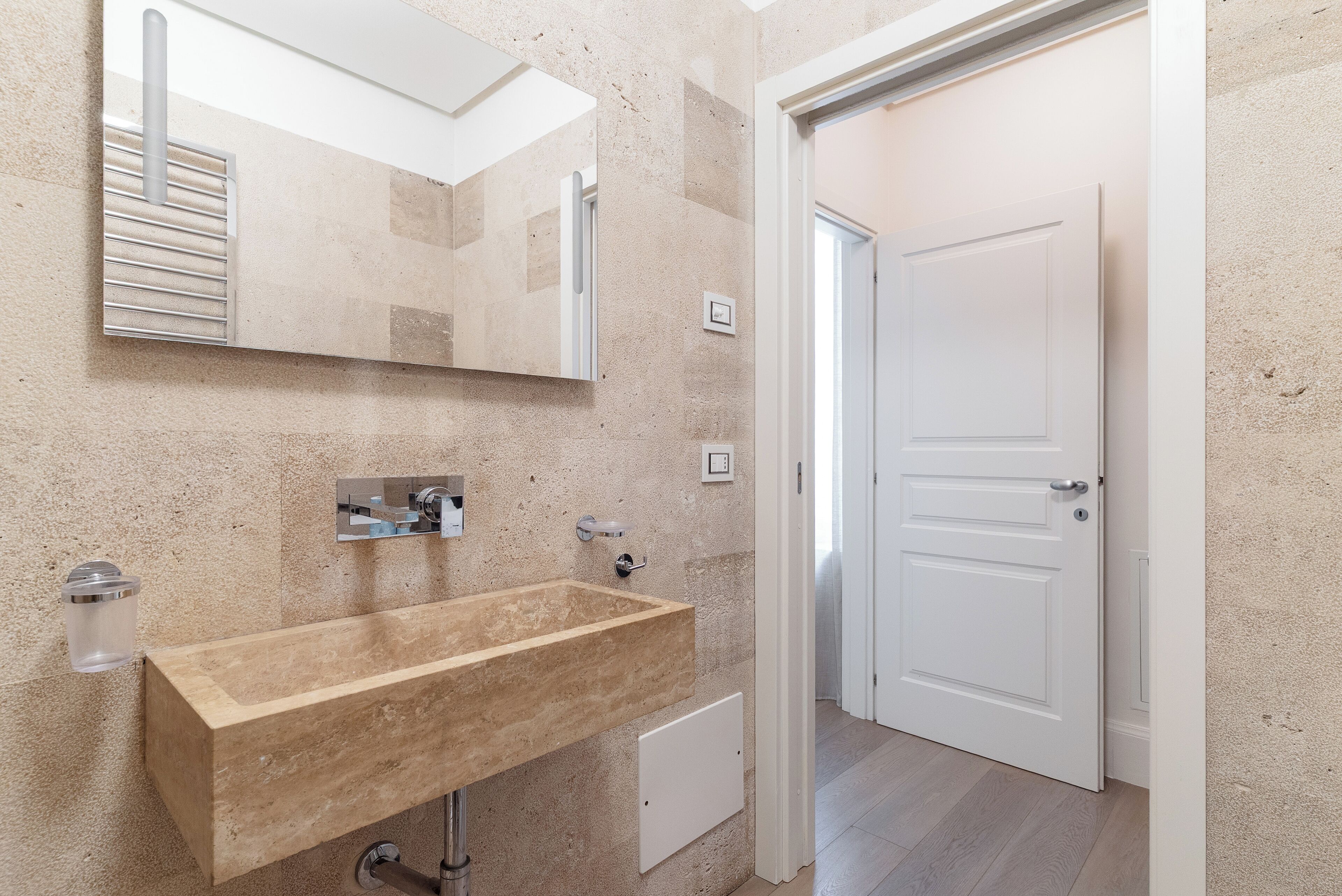 Un baño con lavamanos de mármol color crema, un espejo y una puerta blanca.