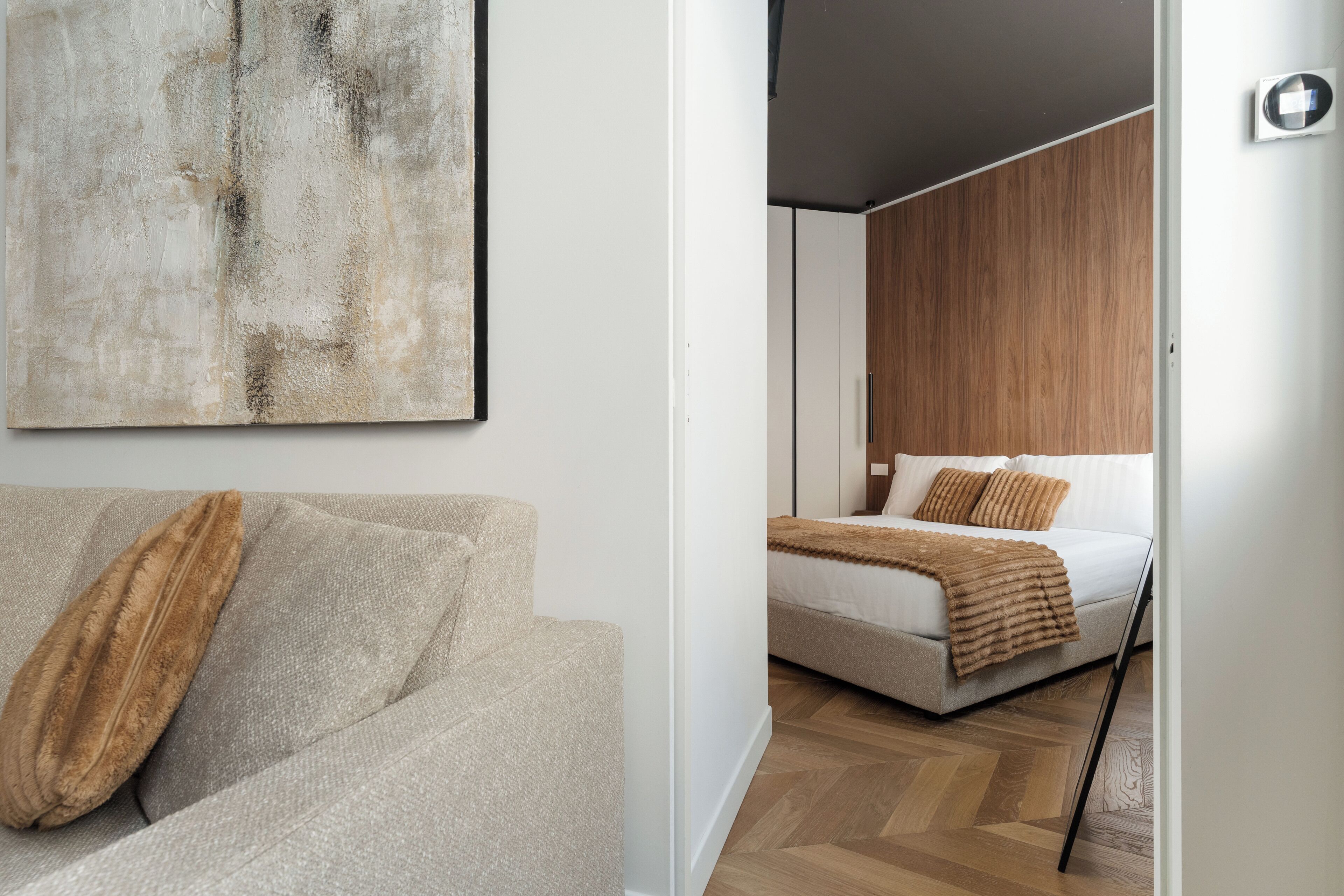 A modern room with a sofa, a bed with a wooden headboard, and a large abstract painting on the wall.