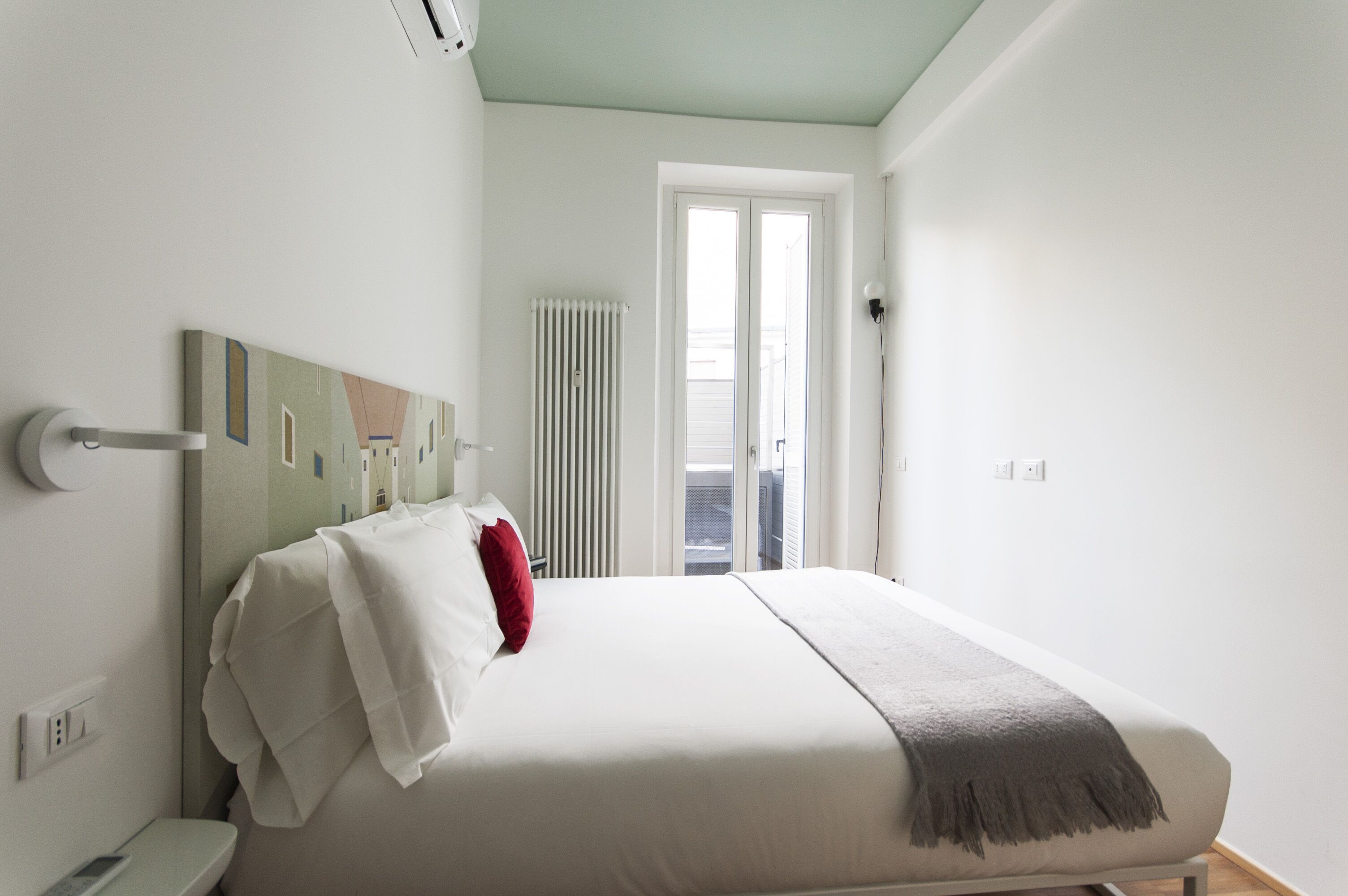 A bedroom with a bed, a radiator, and a door leading to a balcony.