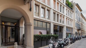 A row of parked scooters along a street with a building featuring large windows and a clear entrance. - Brera Apartments in City Center (Milan)