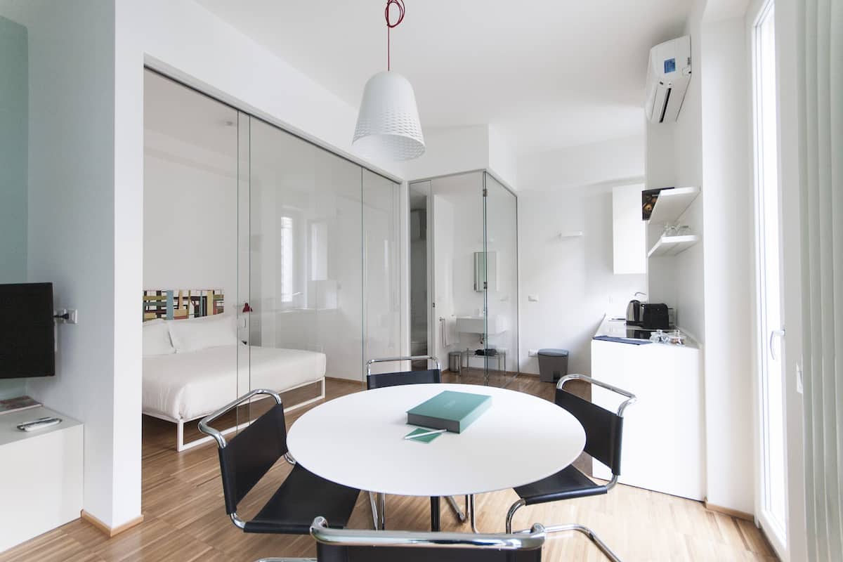 A modern, well-lit room with a round dining table, a sofa, and a kitchen area.