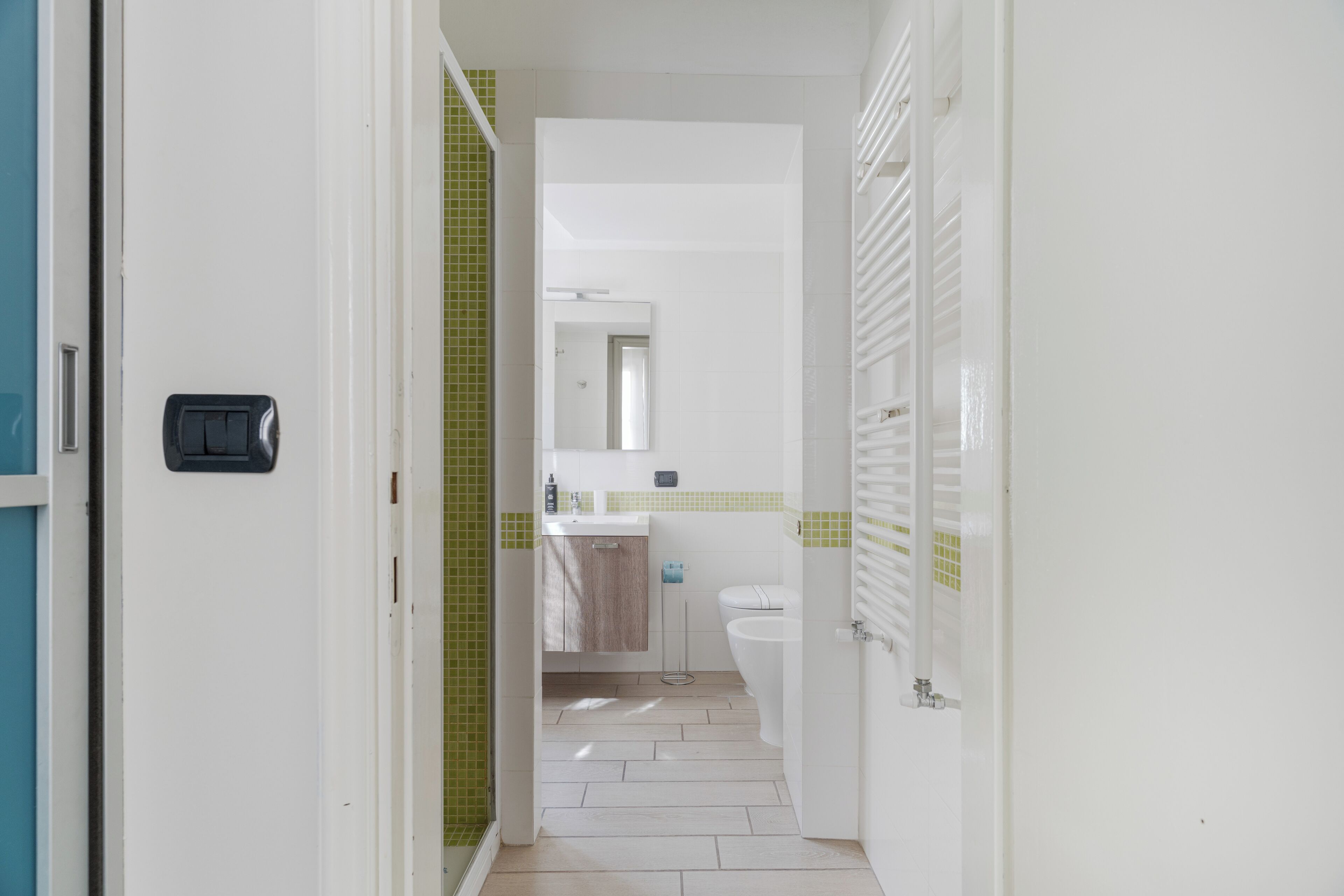 A narrow hallway leading to a bathroom with a toilet, sink, and mirror.