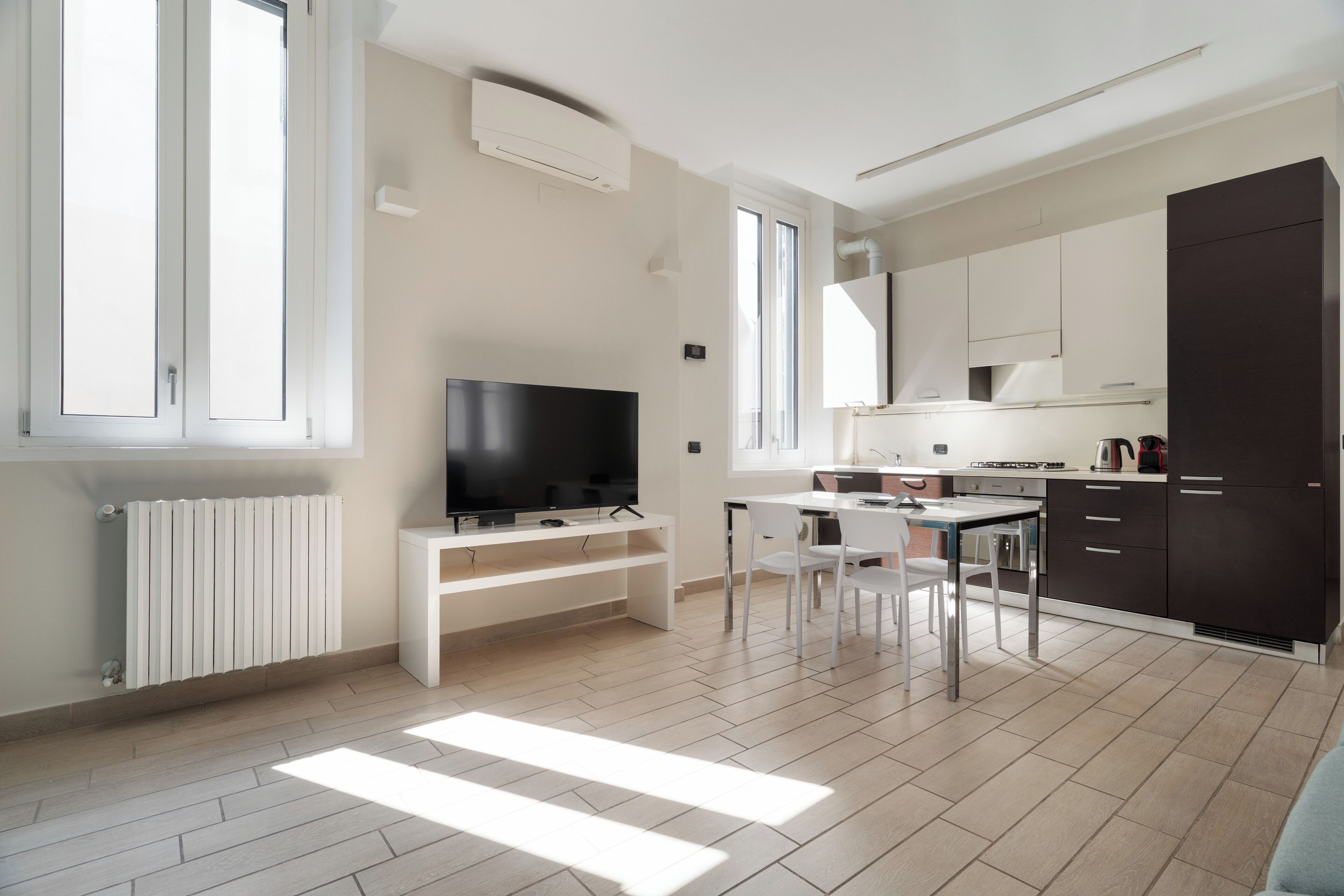 Una cocina moderna con muebles blancos, estufa integrada y un comedor con mesa y sillas.