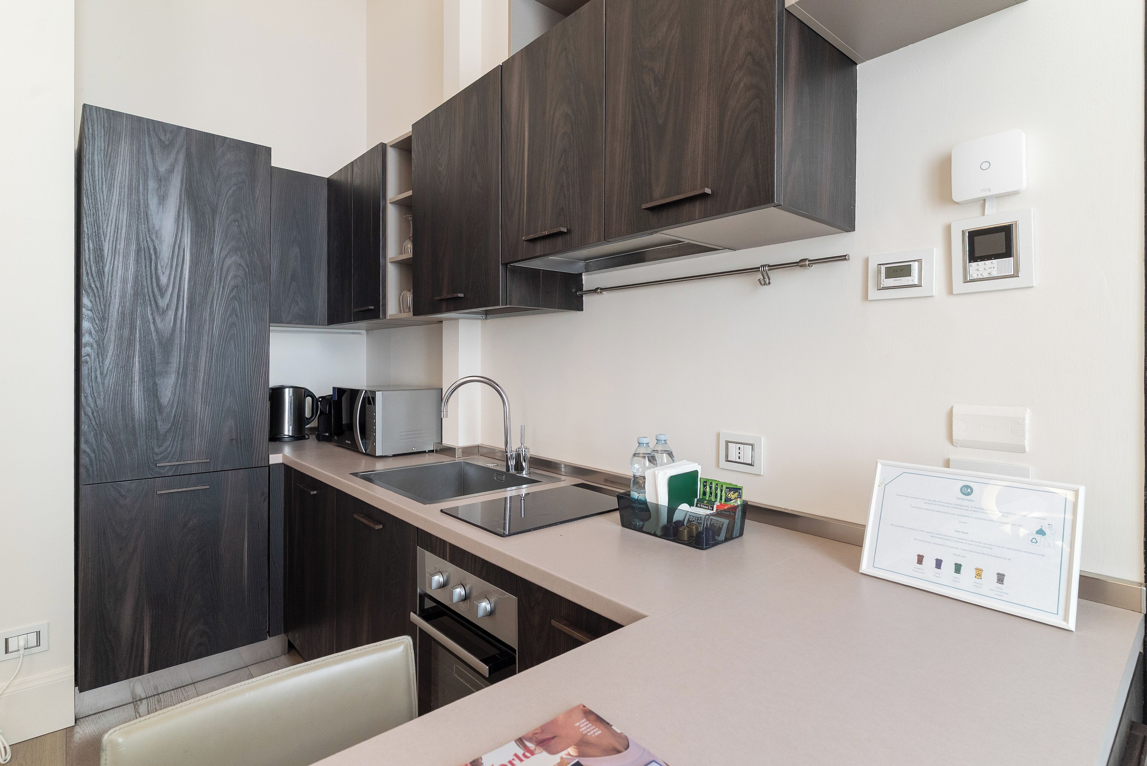 A modern kitchen with dark wood cabinets, stainless steel appliances, a double sink, and a built-in range hood.