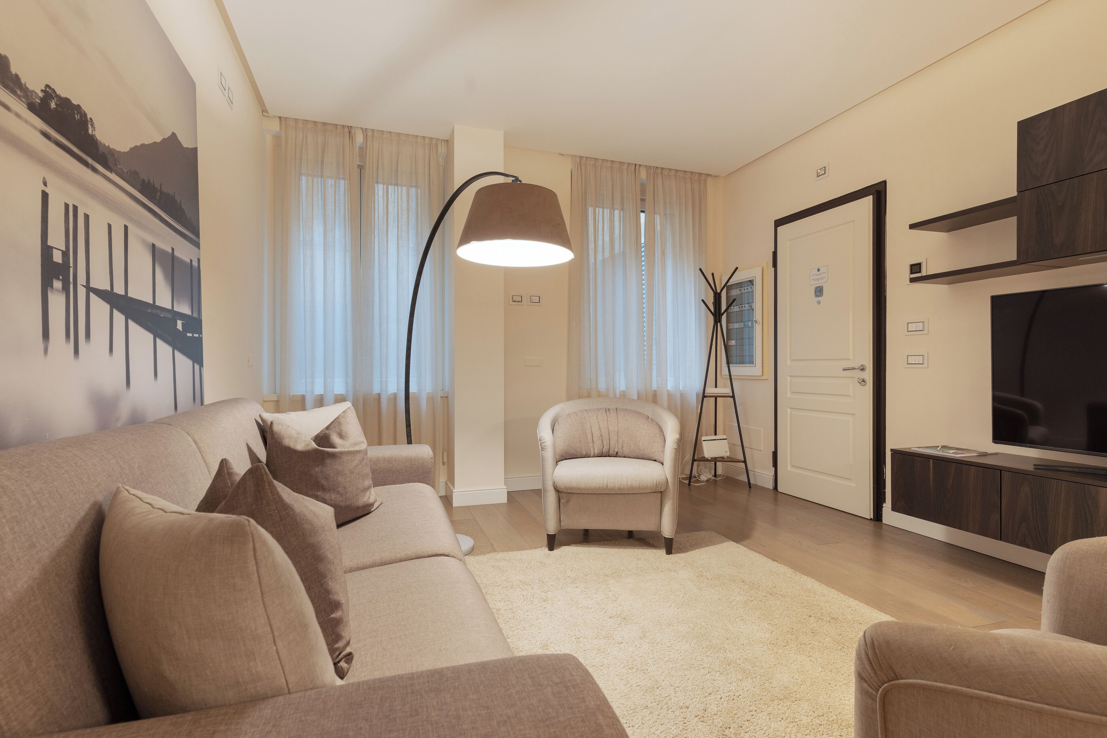 Ein modernes Wohnzimmer mit einer Couch, Sesseln, einer Stehlampe und einem Fernseher.