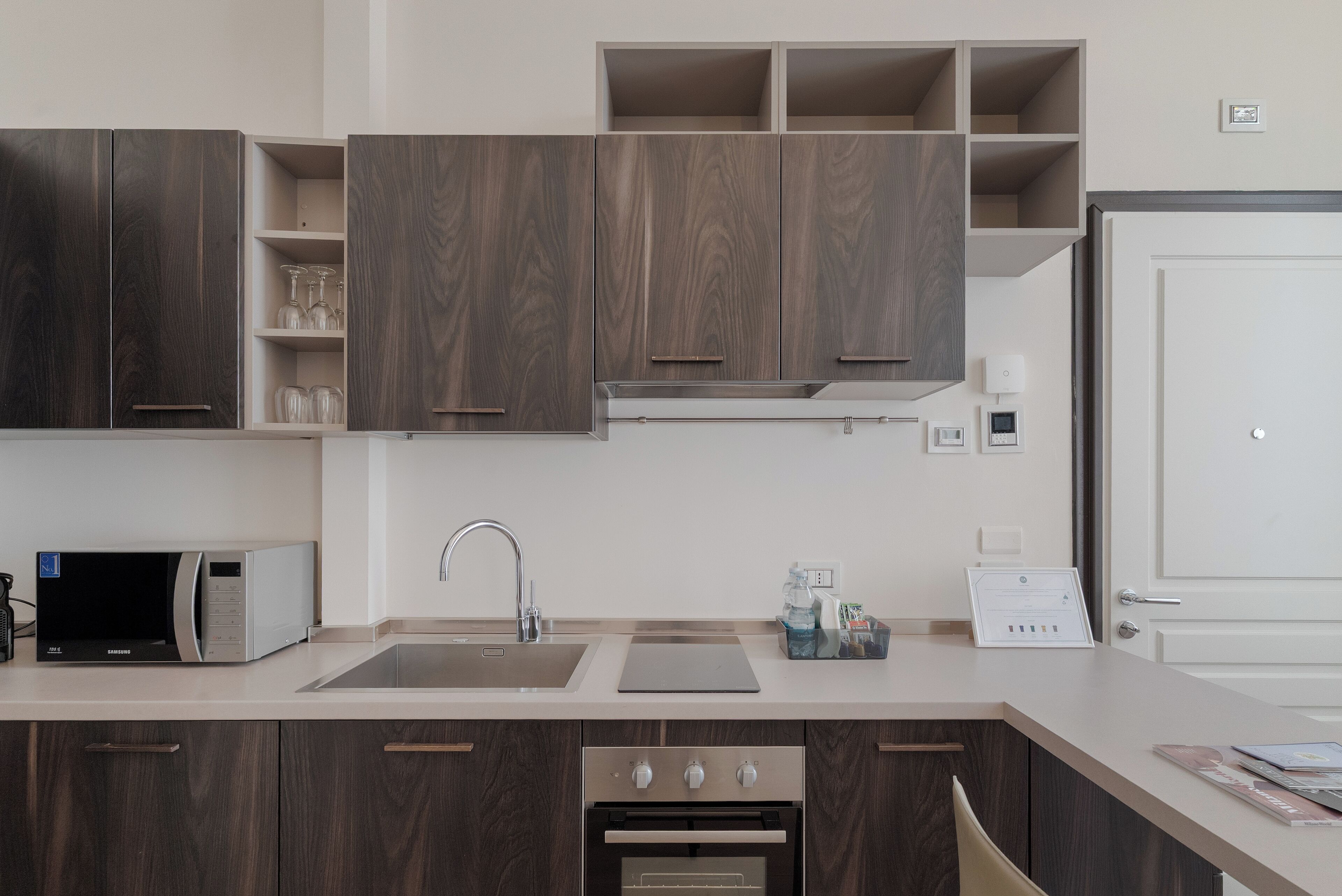 Una cocina moderna con armarios de madera oscura, un lavamanos de acero inoxidable, un microondas y un horno empotrado.