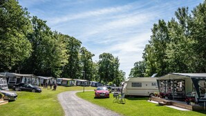 A campsite with RVs and cars parked on a grassy area, surrounded by trees.