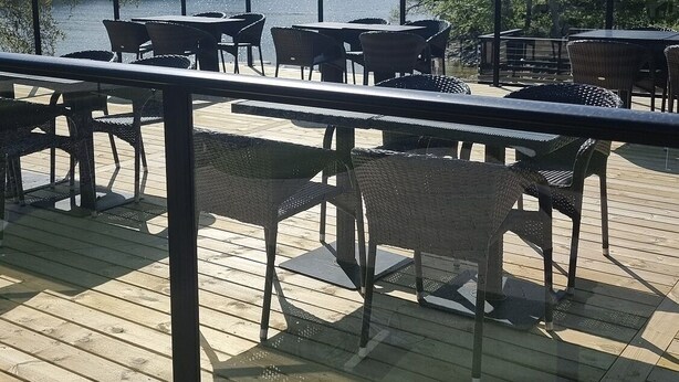 An outdoor deck with wooden flooring and metal railings, overlooking a body of water with trees in the background.