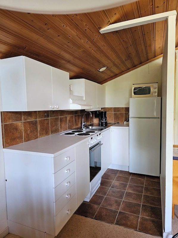 A compact kitchen with white cabinets, a stove, a microwave, and a refrigerator.