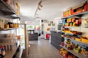 A grocery store interior with shelves stocked with various products, a reception area, and a freezer in the background.