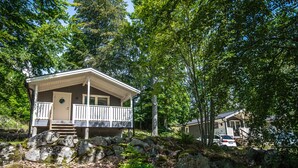 A cabin with a porch and a deck, surrounded by trees and rocks.